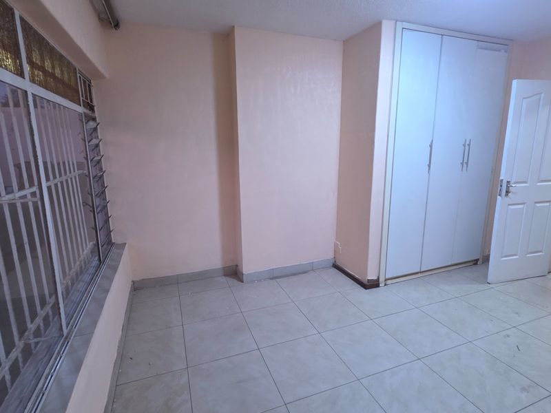 An empty bedroom featuring tiled flooring, a built-in wardrobe, and large windows with security bars.