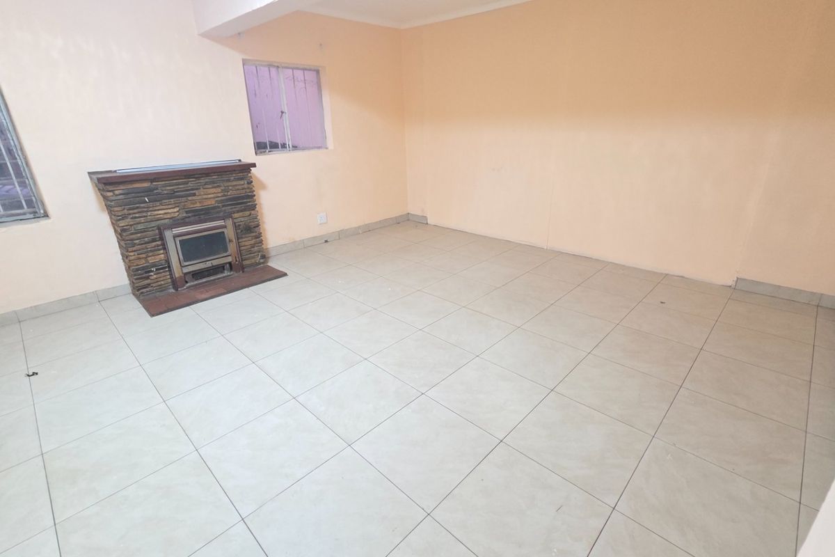 An empty living room featuring tiled flooring and a stone-clad fireplace, offering a blank canvas for renovation and interior design updates.