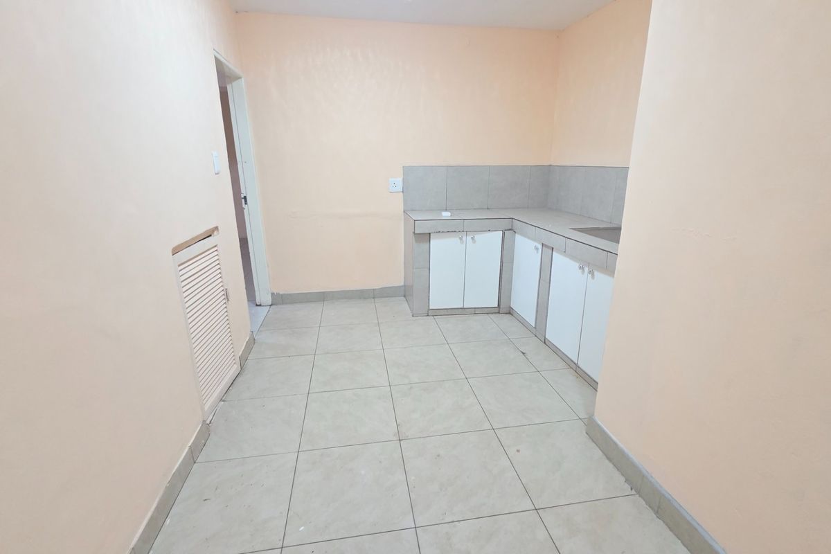 A compact, empty kitchen featuring tiled flooring, built-in base cabinetry with a tiled splashback, and a functional sink area.