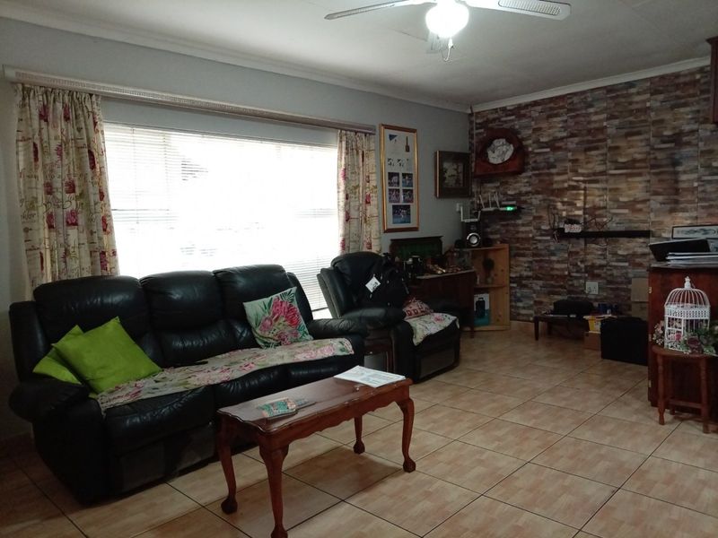A living room featuring tiled flooring, a ceiling fan, and a stone-cladding feature wall with large window access.