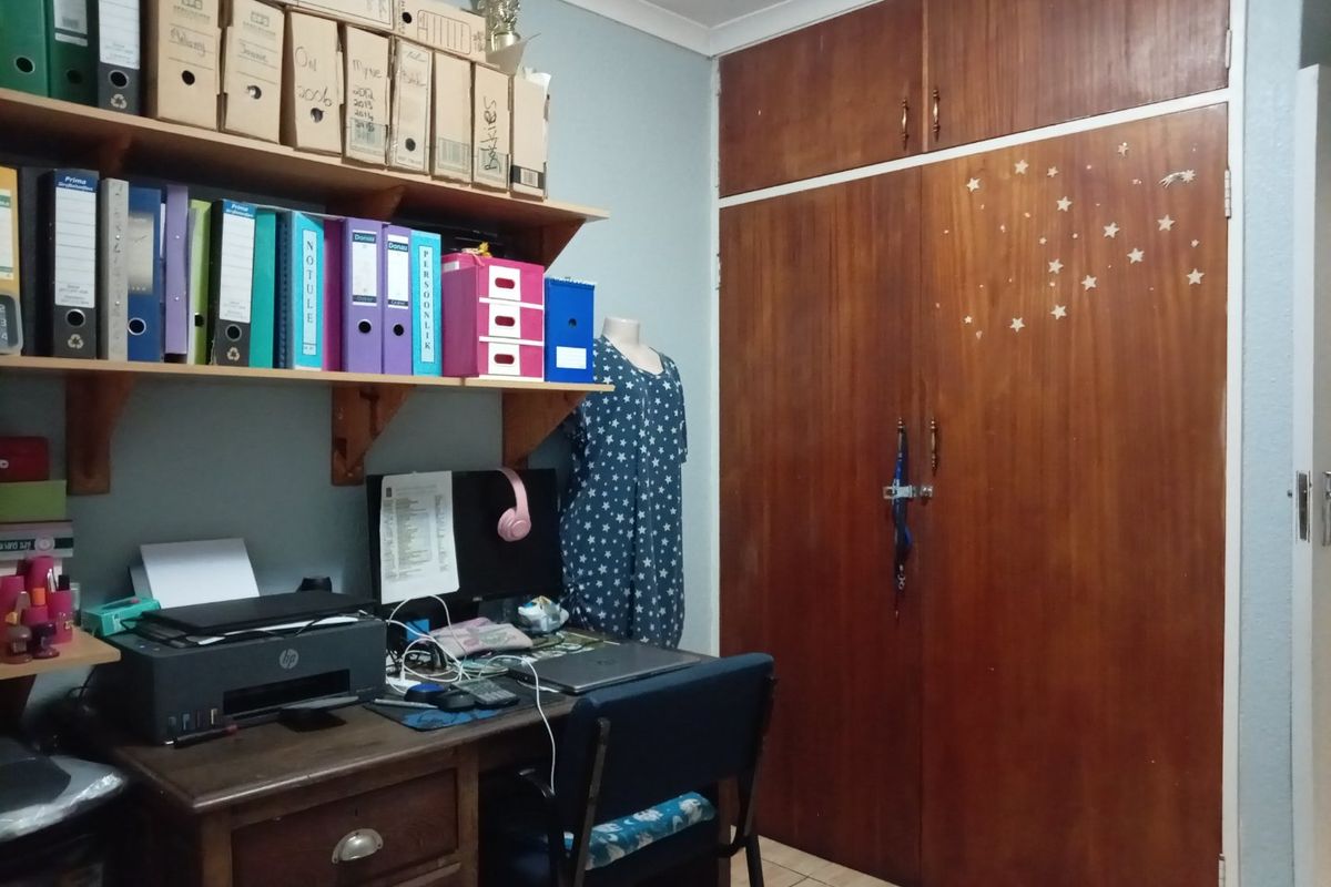 A bedroom featuring built-in wooden cupboards and wall-mounted shelving, currently utilized as a home office space.