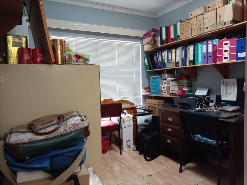 A functional home office space featuring built-in wall shelving, tiled flooring, and window blinds, currently utilized as a workspace.