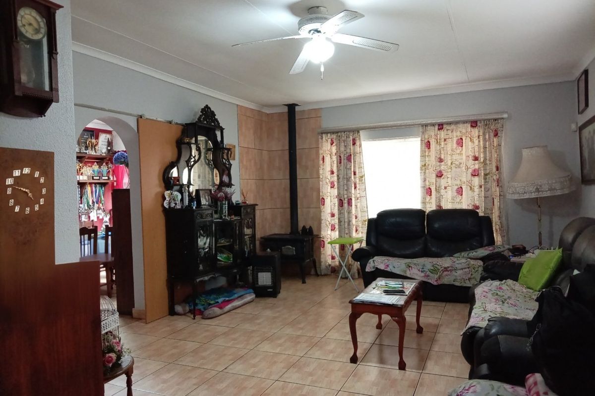 A spacious living room featuring tiled flooring, a ceiling fan, and a built-in wood-burning fireplace, with an arched entryway leading to an adjacent room.