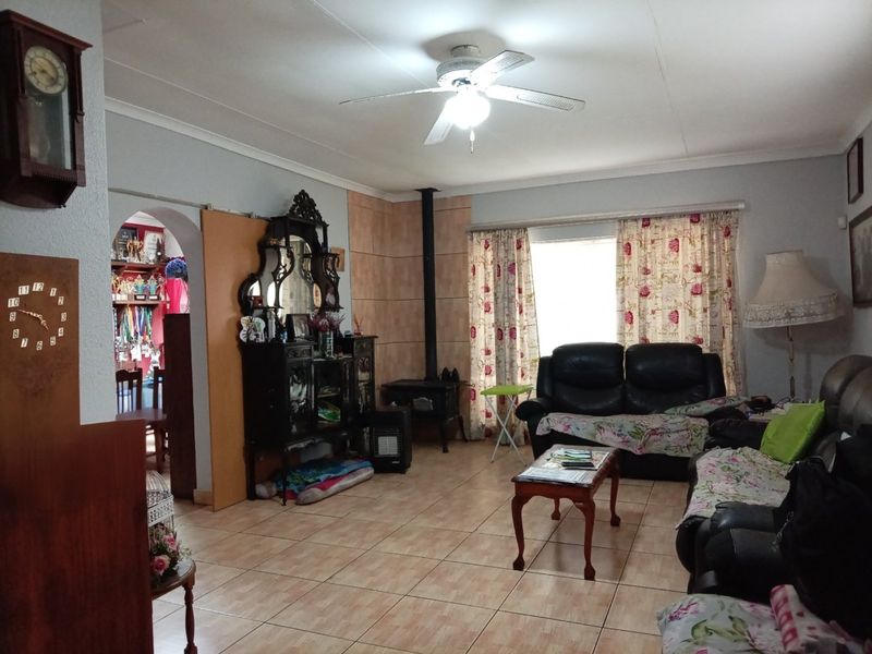 A spacious living room featuring tiled flooring, a ceiling fan, and a built-in wood-burning fireplace, with an arched entryway leading to an adjacent room.