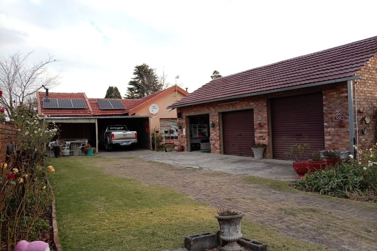 Rear exterior view featuring a brick-faced double garage, attached carport with solar panels, and a paved driveway leading to the garden area.