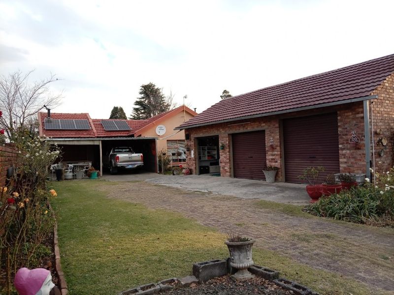 Rear exterior view featuring a brick-faced double garage, attached carport with solar panels, and a paved driveway leading to the garden area.