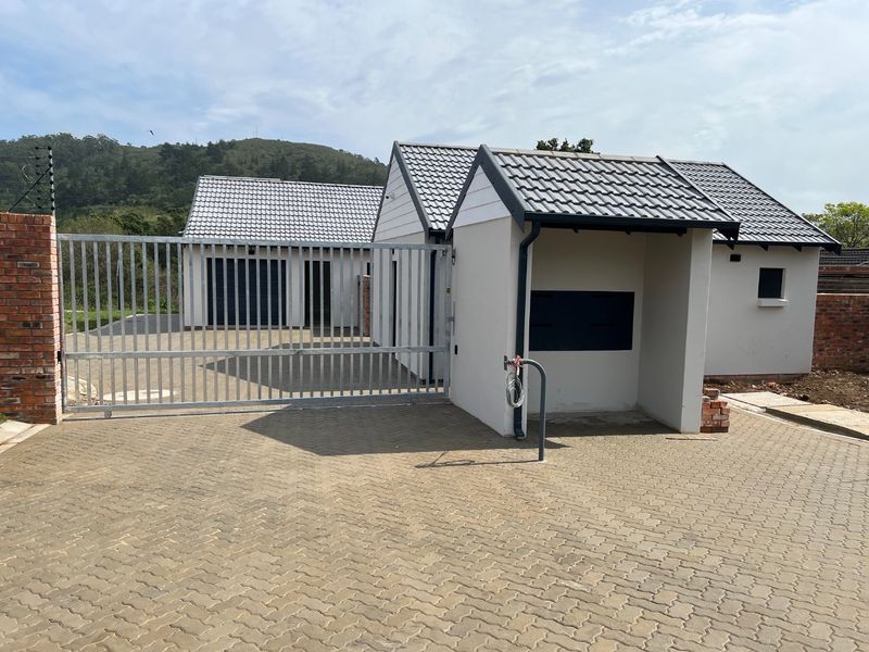 Front exterior view of the property featuring a paved driveway, secure sliding gate, electric fencing, and a modern garage structure.