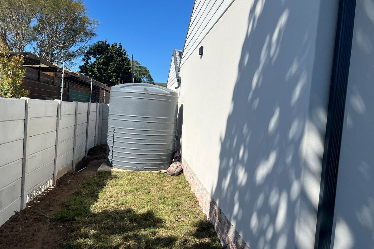 Side exterior area featuring a large water storage tank, precast concrete boundary wall, and plastered building facade with a downpipe.