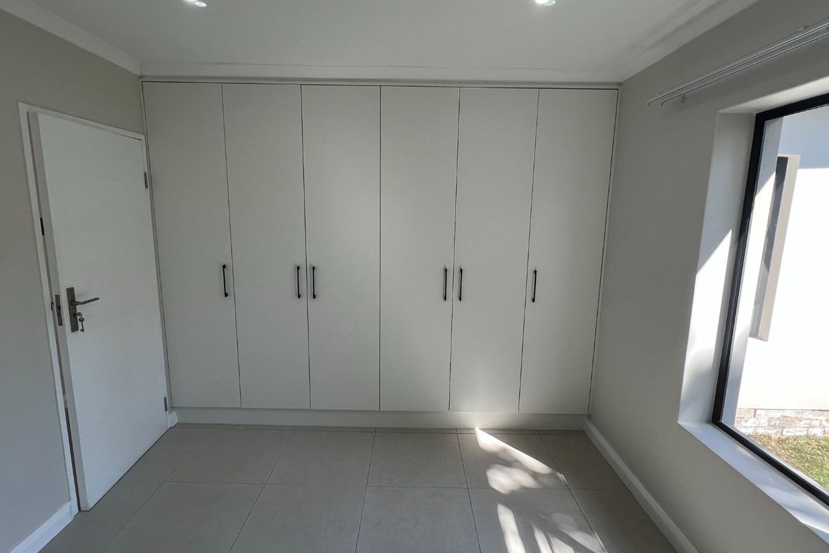 A bright, empty bedroom featuring modern built-in cupboards, neutral tiled flooring, and recessed downlighting, offering a clean and versatile living space.