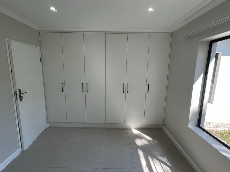 A bright, empty bedroom featuring modern built-in cupboards, neutral tiled flooring, and recessed downlighting, offering a clean and versatile living space.