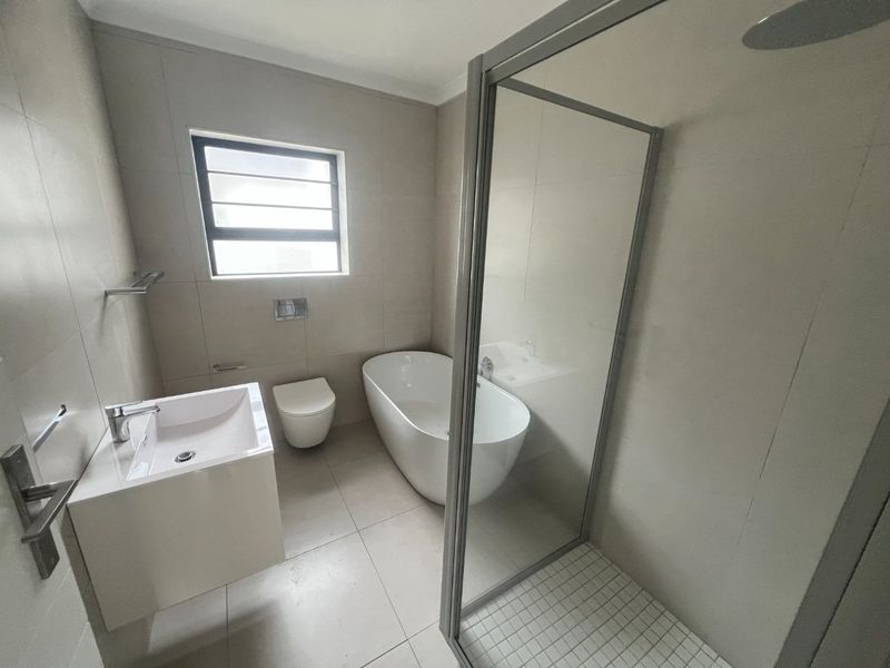 Modern bathroom featuring a freestanding bathtub, glass-enclosed shower, wall-hung toilet, and a sleek vanity basin with neutral floor-to-ceiling tiling.
