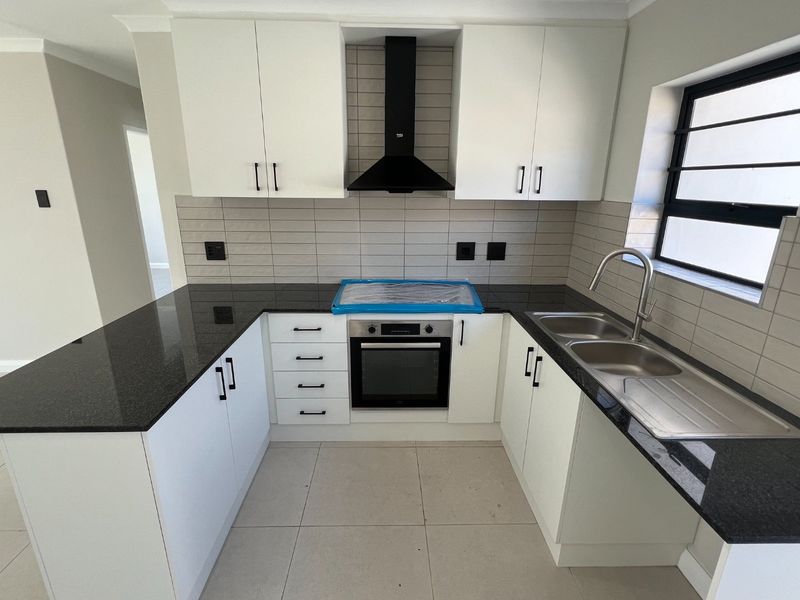 A modern, clean kitchen featuring white cabinetry, black granite countertops, a built-in oven, extractor fan, and a double sink with tiled backsplash.