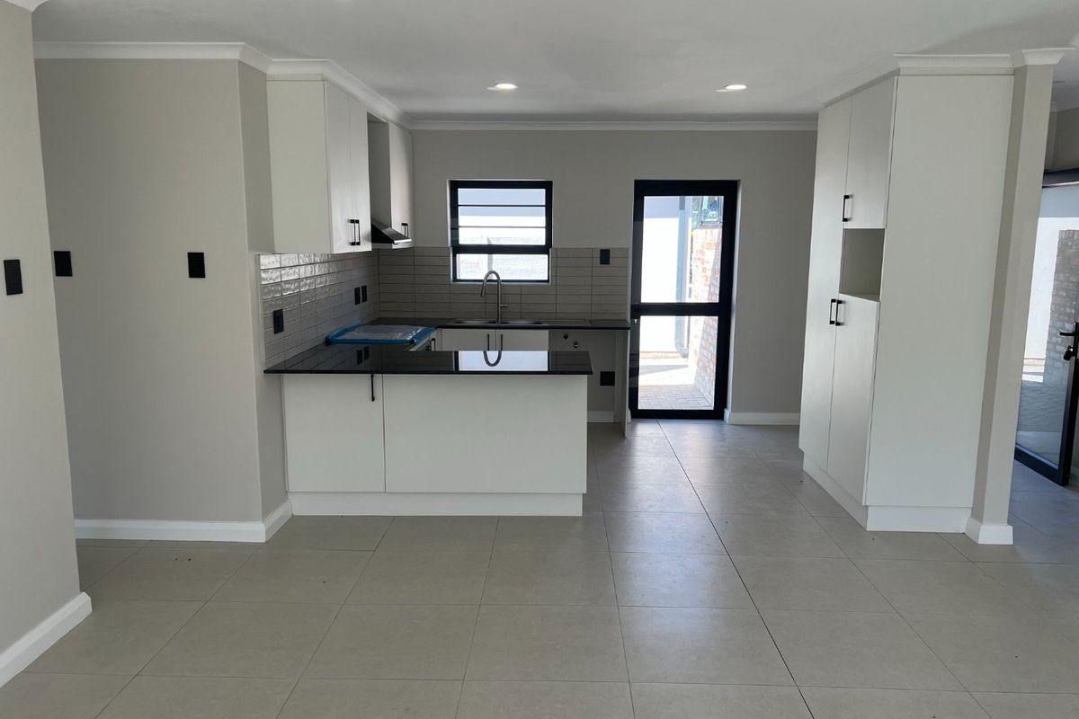Modern, empty kitchen featuring white cabinetry, black granite countertops, tiled backsplash, and direct access to an outdoor area.