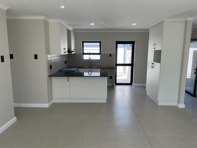 Modern, empty kitchen featuring white cabinetry, black granite countertops, tiled backsplash, and direct access to an outdoor area.