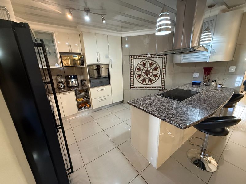 Modern kitchen featuring glossy cabinetry, granite countertops, a central island with an induction cooktop, and a decorative mosaic wall accent.