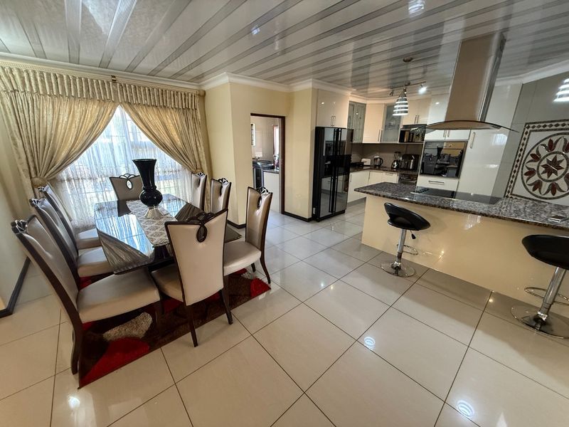 Spacious open-plan kitchen and dining area featuring granite countertops, modern built-in appliances, glossy cabinetry, and polished ceramic floor tiles throughout.
