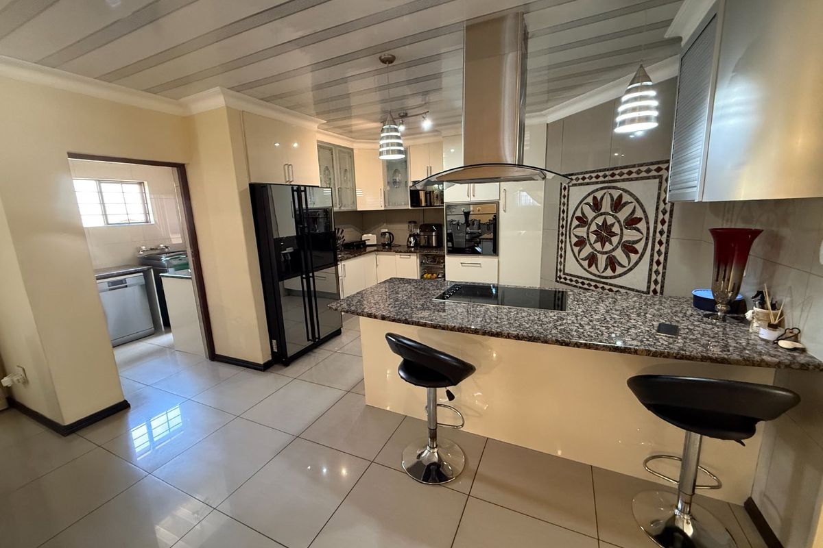 Modern kitchen featuring granite countertops, built-in oven, extractor fan, and a decorative mosaic backsplash, with an adjacent scullery area.