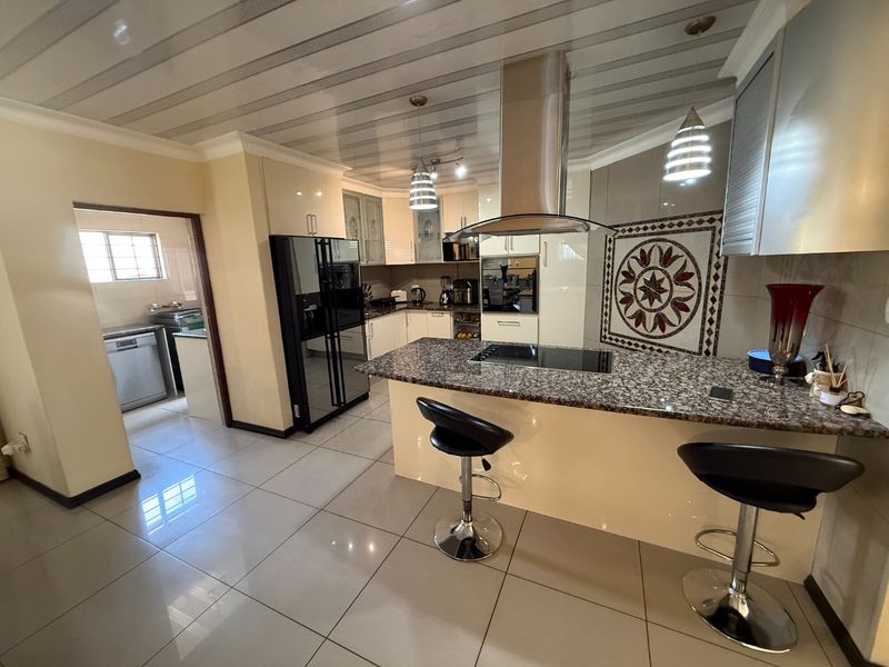 Modern kitchen featuring granite countertops, built-in oven, extractor fan, and a decorative mosaic backsplash, with an adjacent scullery area.