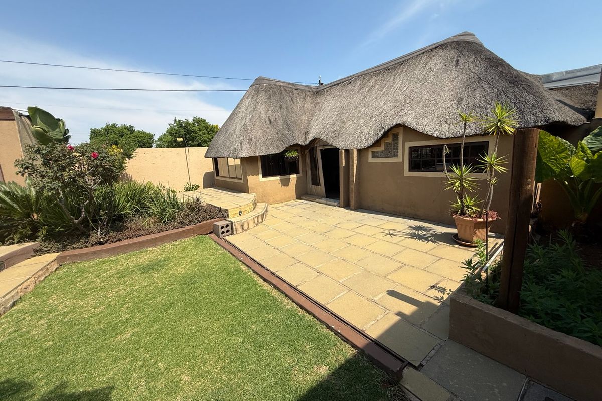 Rear view of a house featuring a traditional thatched roof, a paved patio area, and a well-maintained garden space.