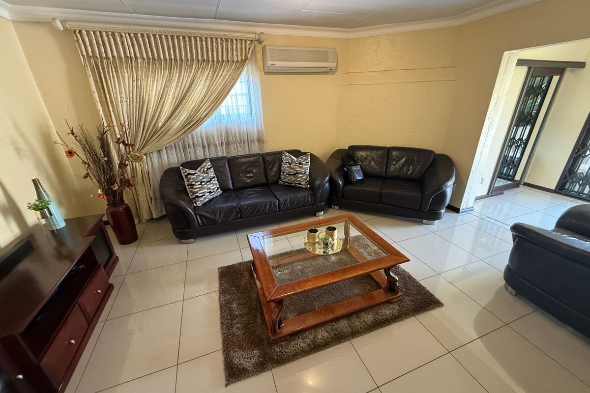 A living room featuring tiled flooring, a wall-mounted air conditioning unit, and access to an adjacent area through a security gate.