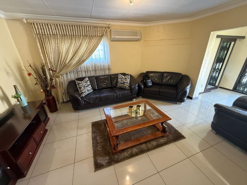 A living room featuring tiled flooring, a wall-mounted air conditioning unit, and access to an adjacent area through a security gate.