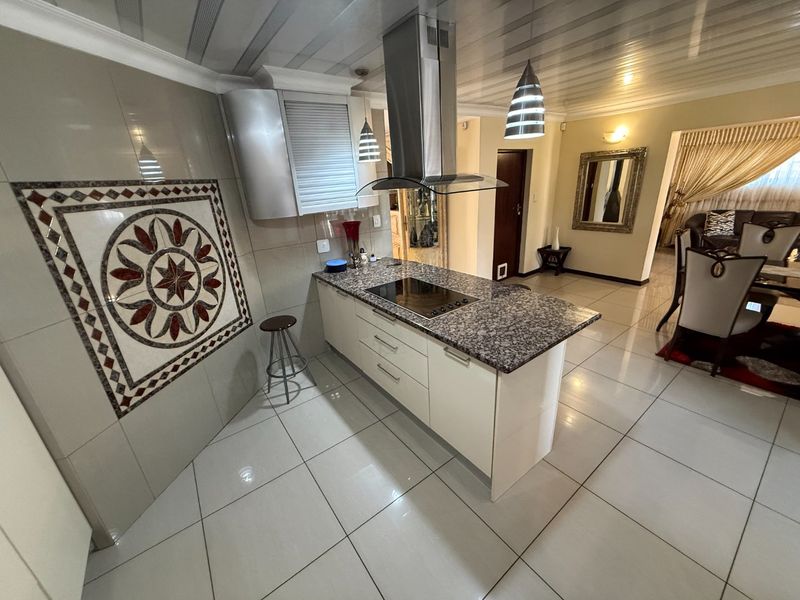 Modern kitchen featuring a granite-topped island with built-in induction hob, stainless steel extractor fan, and decorative wall mosaic tiling.