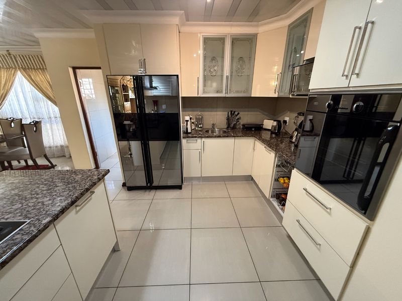 Modern kitchen featuring high-gloss cabinetry, granite countertops, integrated appliances, and large format floor tiles, offering a clean and functional culinary space.