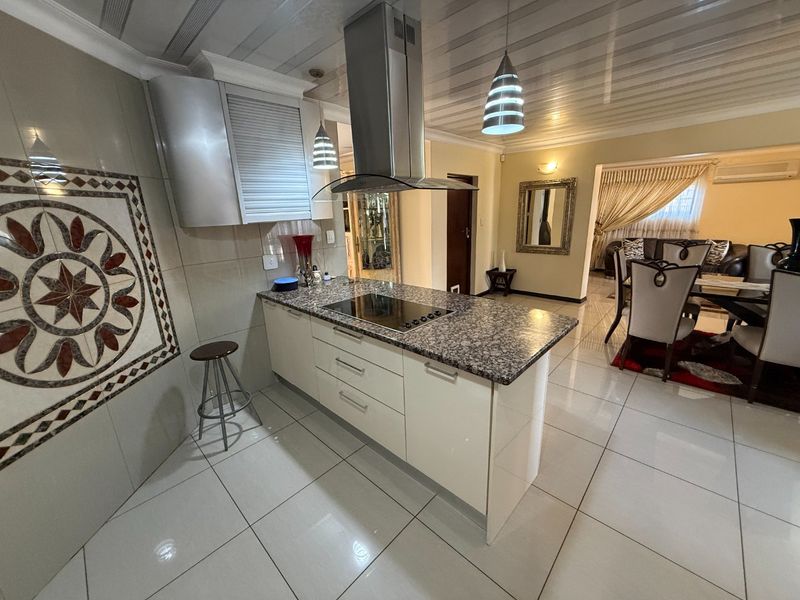 Open-plan kitchen featuring a central island with granite countertops, induction hob, and stainless steel extractor fan, flowing into the adjacent dining and living area.