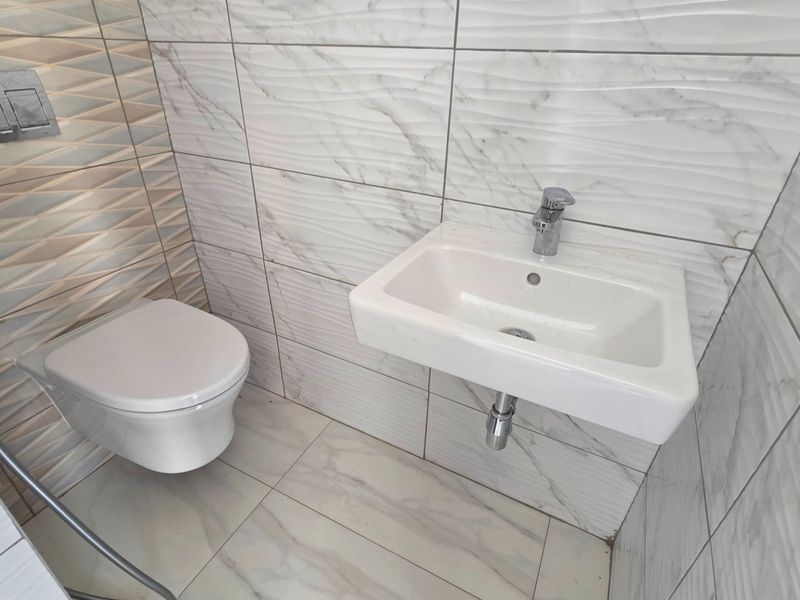 A modern, compact bathroom featuring wall-mounted sanitary ware, marble-effect textured wall tiles, and a sleek chrome faucet.