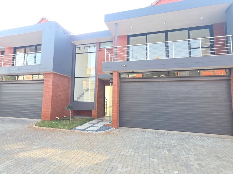 Modern townhouse exterior featuring a brick facade, double garage doors, and an upper-level balcony with stainless steel railings.