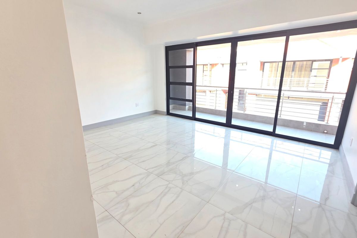 A bright, empty living room featuring large-format marble-look floor tiles and expansive black-framed sliding glass doors leading to an outdoor balcony.
