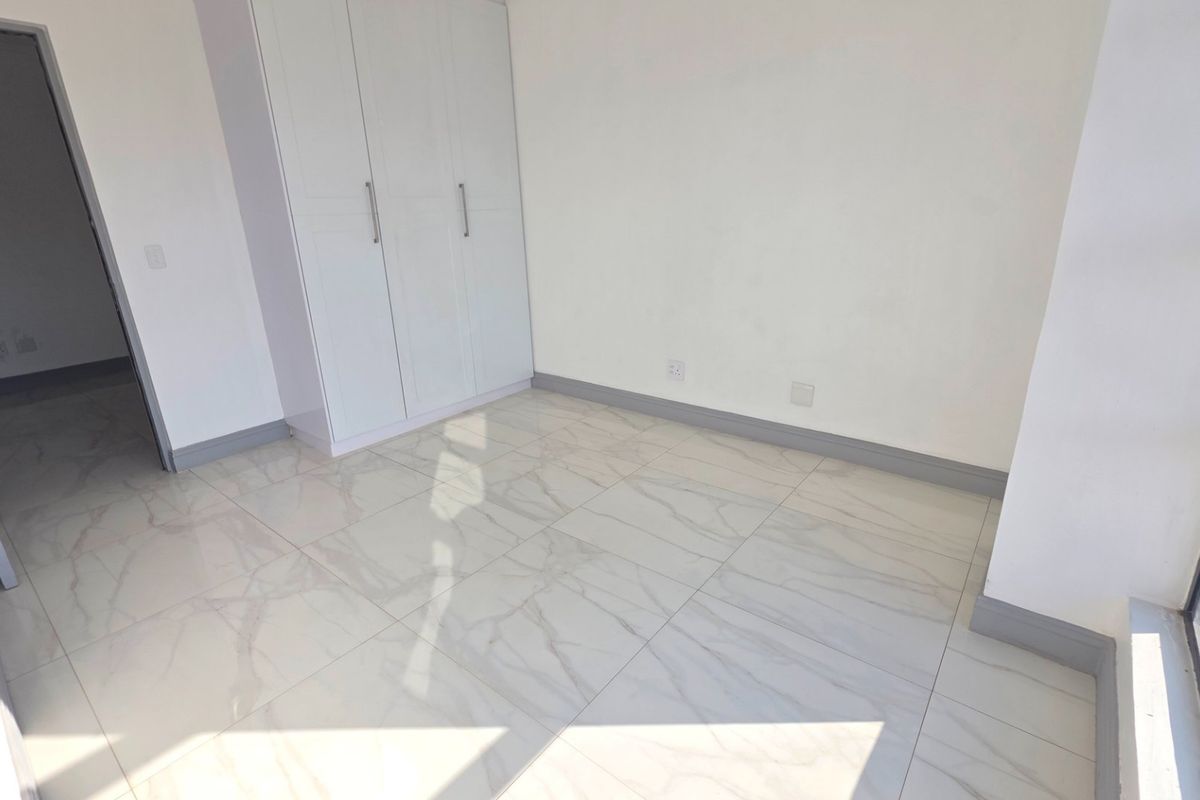 A bright, empty bedroom featuring modern marble-look floor tiles and built-in white cupboards, offering a clean and neutral space ready for personalization.
