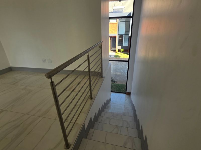 A bright, modern hallway featuring a staircase with a stainless steel balustrade and large windows providing natural light and views of the exterior.