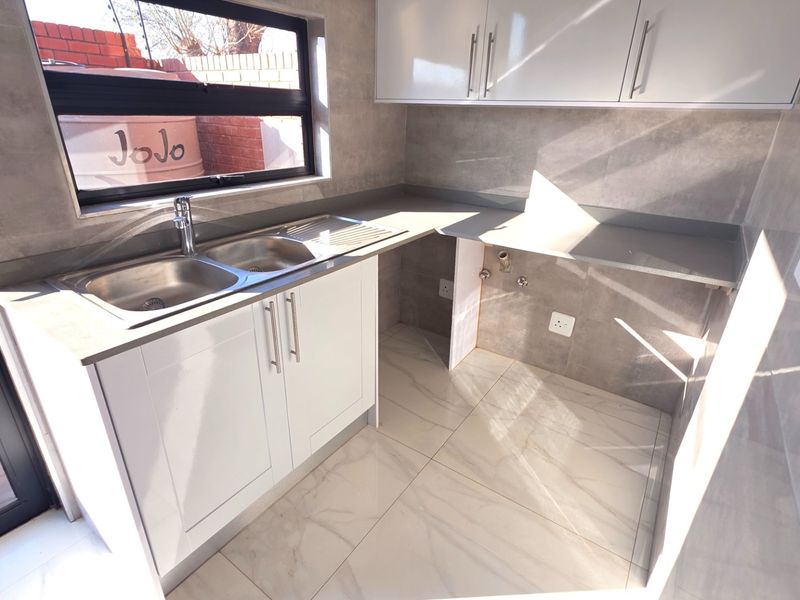 A modern, clean scullery featuring white cabinetry, stone-look countertops, double sink, and plumbing connections for laundry or kitchen appliances.
