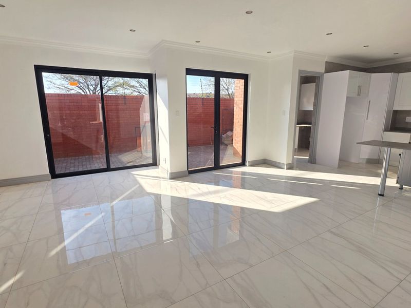 Spacious open-plan living and kitchen area featuring polished porcelain tiles, modern cabinetry, and large glass doors leading to an outdoor patio.