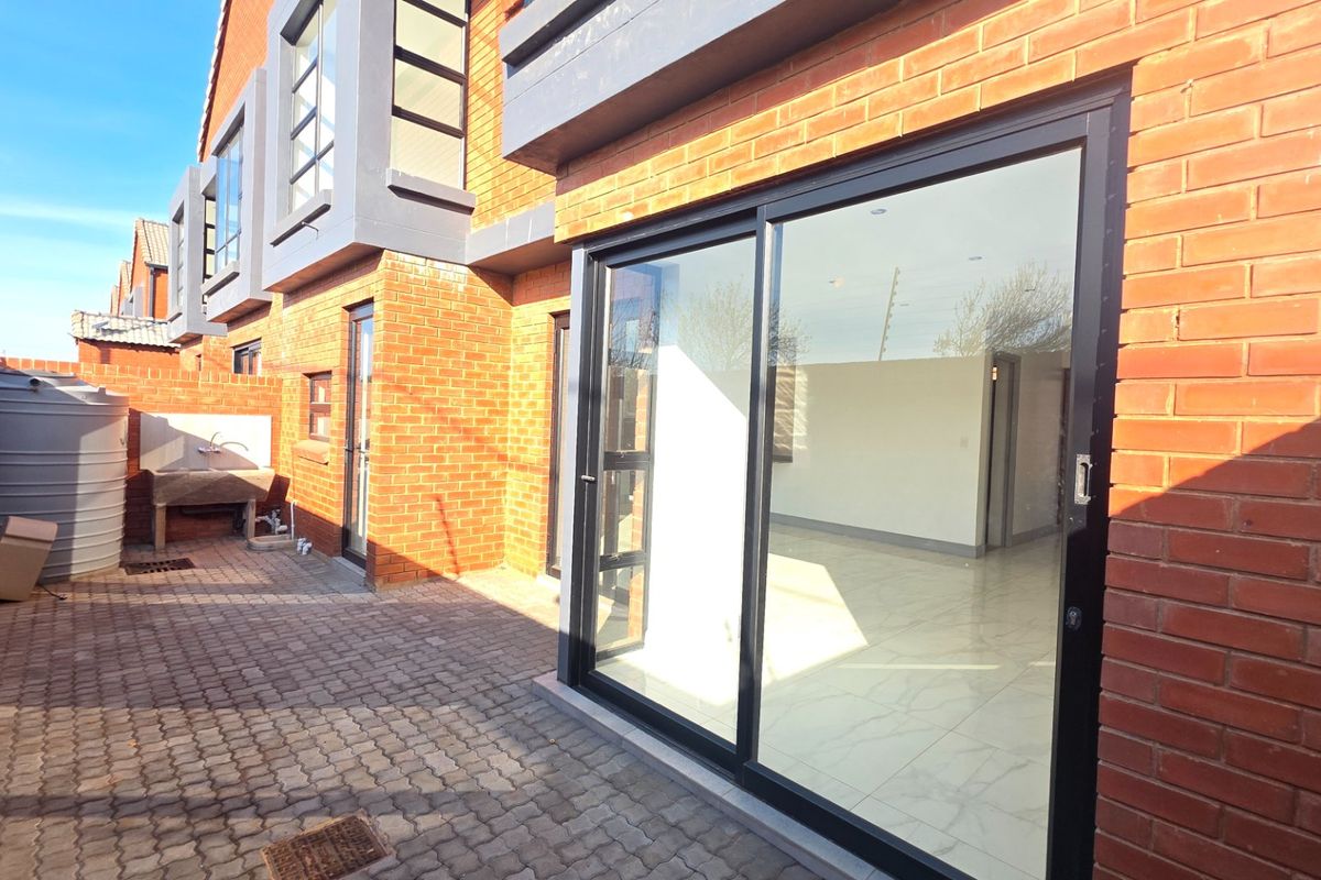 Rear exterior view of the townhouse featuring a paved patio, sliding glass doors, and a functional outdoor utility area with a water tank.