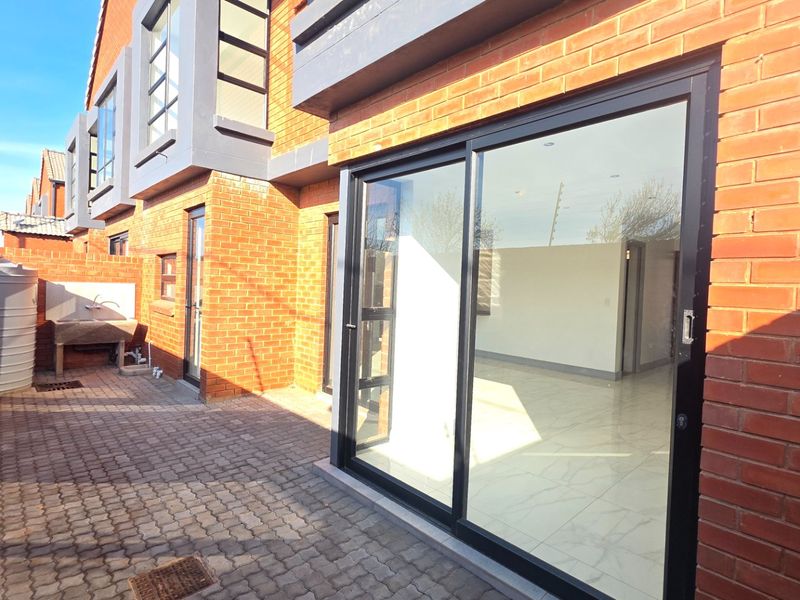 Rear exterior view of the townhouse featuring a paved patio, sliding glass doors, and a functional outdoor utility area with a water tank.