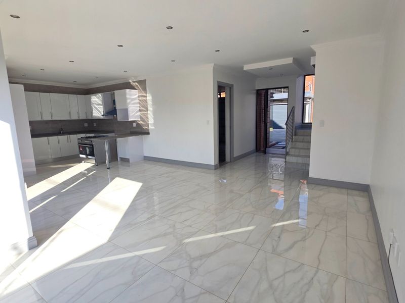 Spacious open-plan living area featuring modern marble-look tiled flooring, recessed lighting, and a sleek kitchen with built-in cabinetry and gas stove.