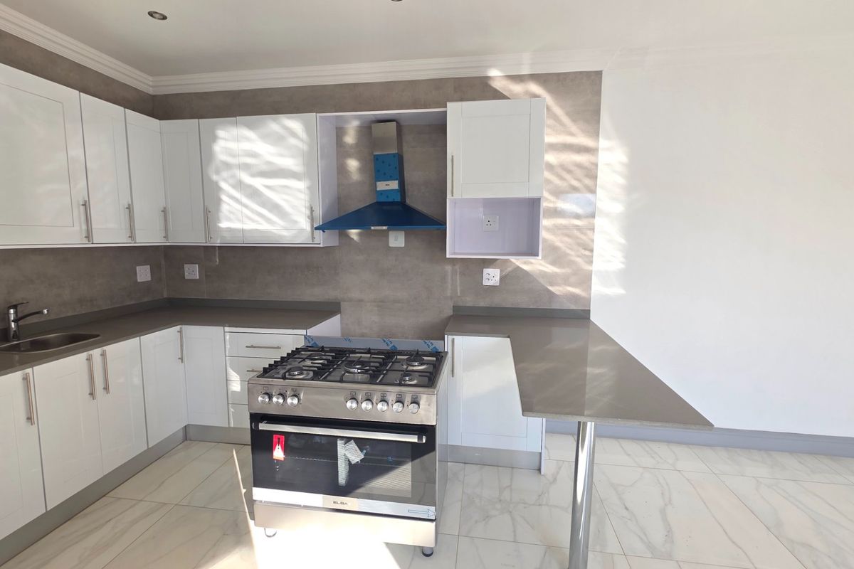 Modern kitchen featuring white shaker-style cabinetry, stone-look countertops, a stainless steel gas stove with extractor, and elegant marble-look floor tiles.