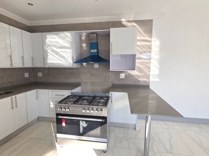 Modern kitchen featuring white shaker-style cabinetry, stone-look countertops, a stainless steel gas stove with extractor, and elegant marble-look floor tiles.