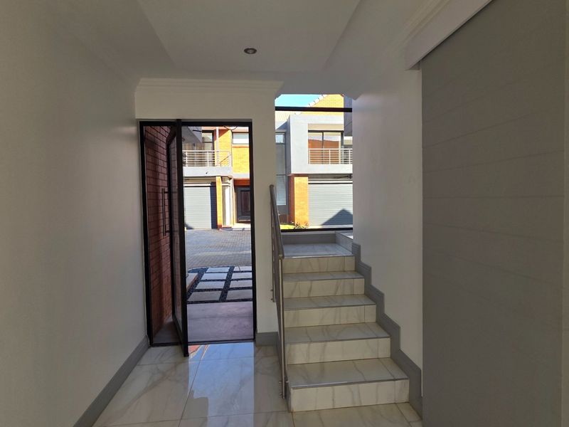 Bright entrance hall featuring tiled flooring, a modern staircase with stainless steel balustrade, and direct access to the front exterior.
