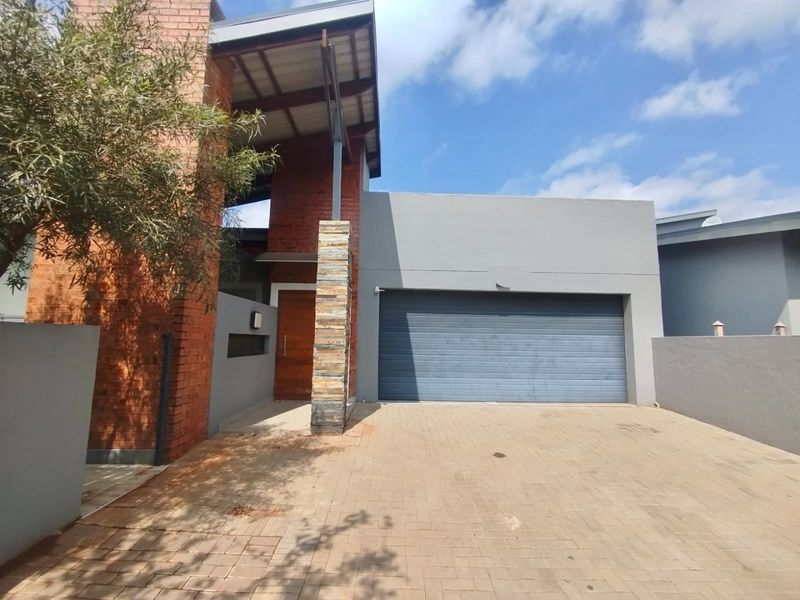 Modern front elevation featuring a combination of face brick and grey render, stone-clad pillar, timber entrance door, and a paved driveway with double garage.
