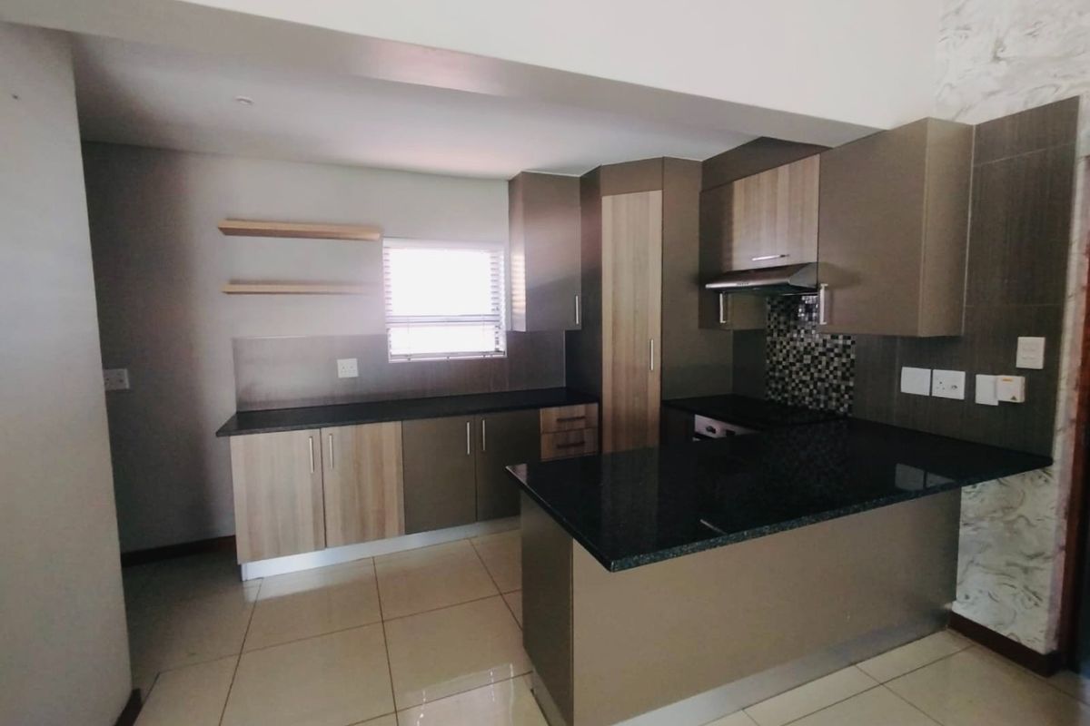 Modern kitchen featuring sleek built-in cabinetry, granite countertops, a mosaic tile backsplash, and an integrated extractor fan, offering a clean and functional workspace.
