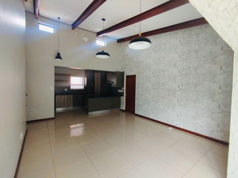 Spacious open-plan living and kitchen area featuring high ceilings with exposed timber beams, tiled floors, and a modern kitchen layout.