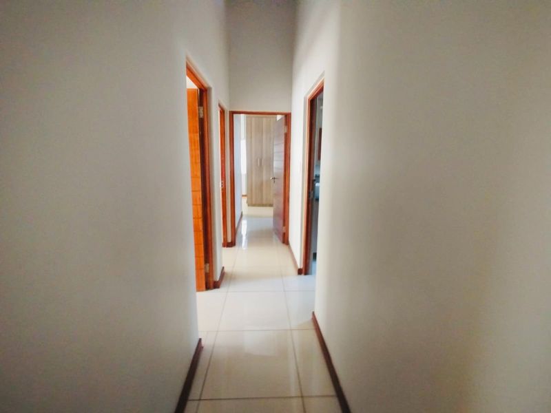 A clean, well-lit hallway featuring neutral tiled flooring and wooden door frames leading to multiple rooms with built-in storage.