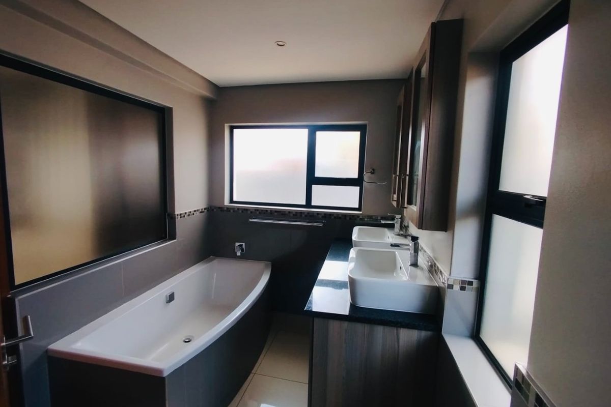 Modern bathroom featuring a built-in bathtub, double vanity with granite countertop, and large frosted windows providing natural light.