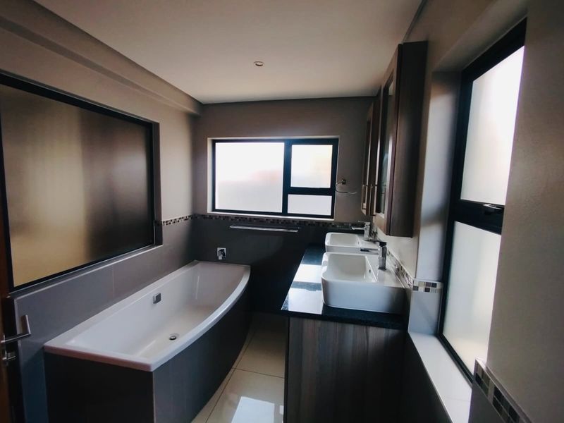 Modern bathroom featuring a built-in bathtub, double vanity with granite countertop, and large frosted windows providing natural light.