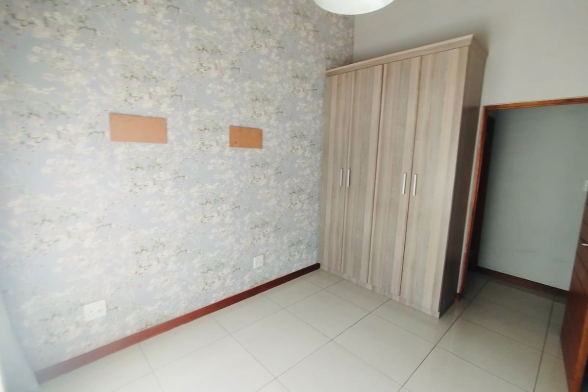 A bedroom featuring tiled flooring, floral wallpaper, and a built-in wardrobe, with visible wall patches requiring minor cosmetic repair.