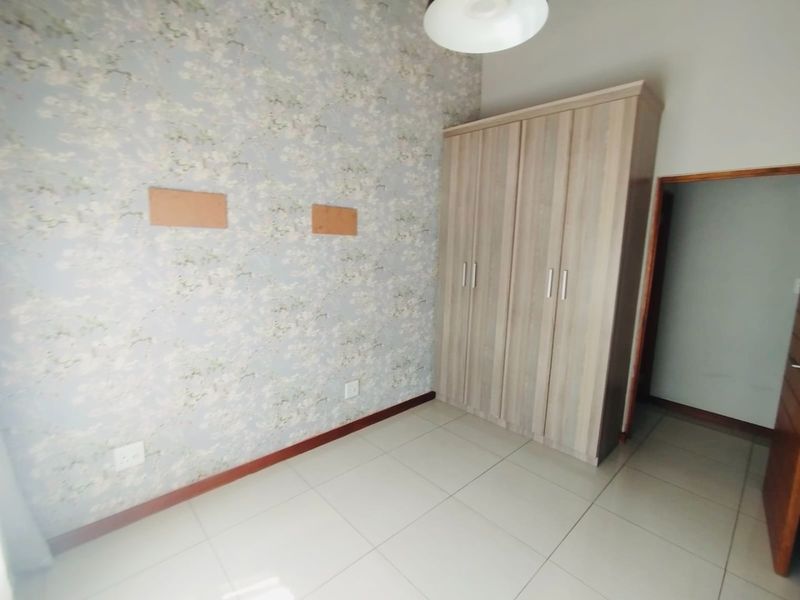 A bedroom featuring tiled flooring, floral wallpaper, and a built-in wardrobe, with visible wall patches requiring minor cosmetic repair.