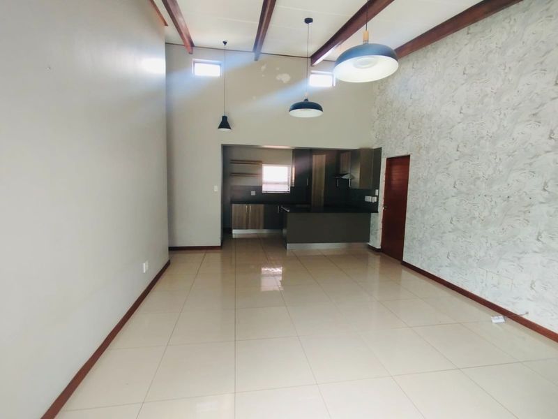 Spacious open-plan living and kitchen area featuring high ceilings with exposed timber beams, tiled flooring, and a modern kitchen with built-in cabinetry.